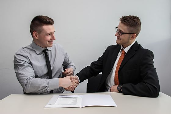 Duas pessoas apertando as mãos sobre a mesa, com um contrato aberto entre elas.
