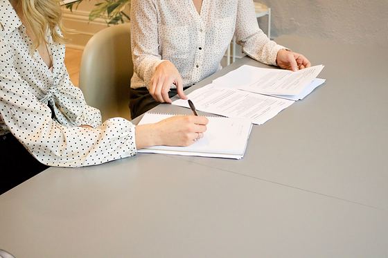 Duas pessoas sentadas à mesa preenchendo e conferindo documentos impressos.